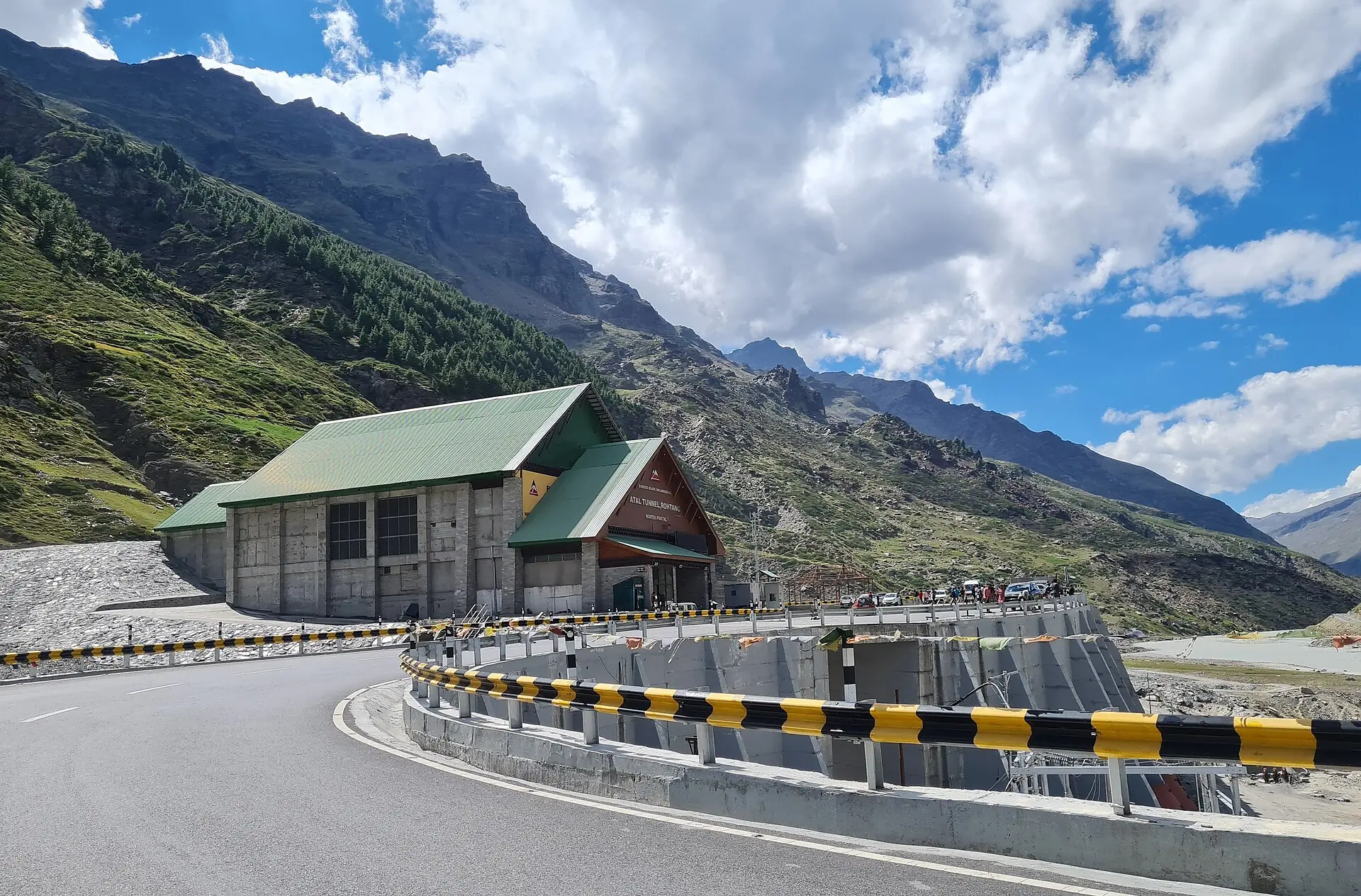 Road curving into the portal of the Atal Tunnel beneath steep mountain slopes