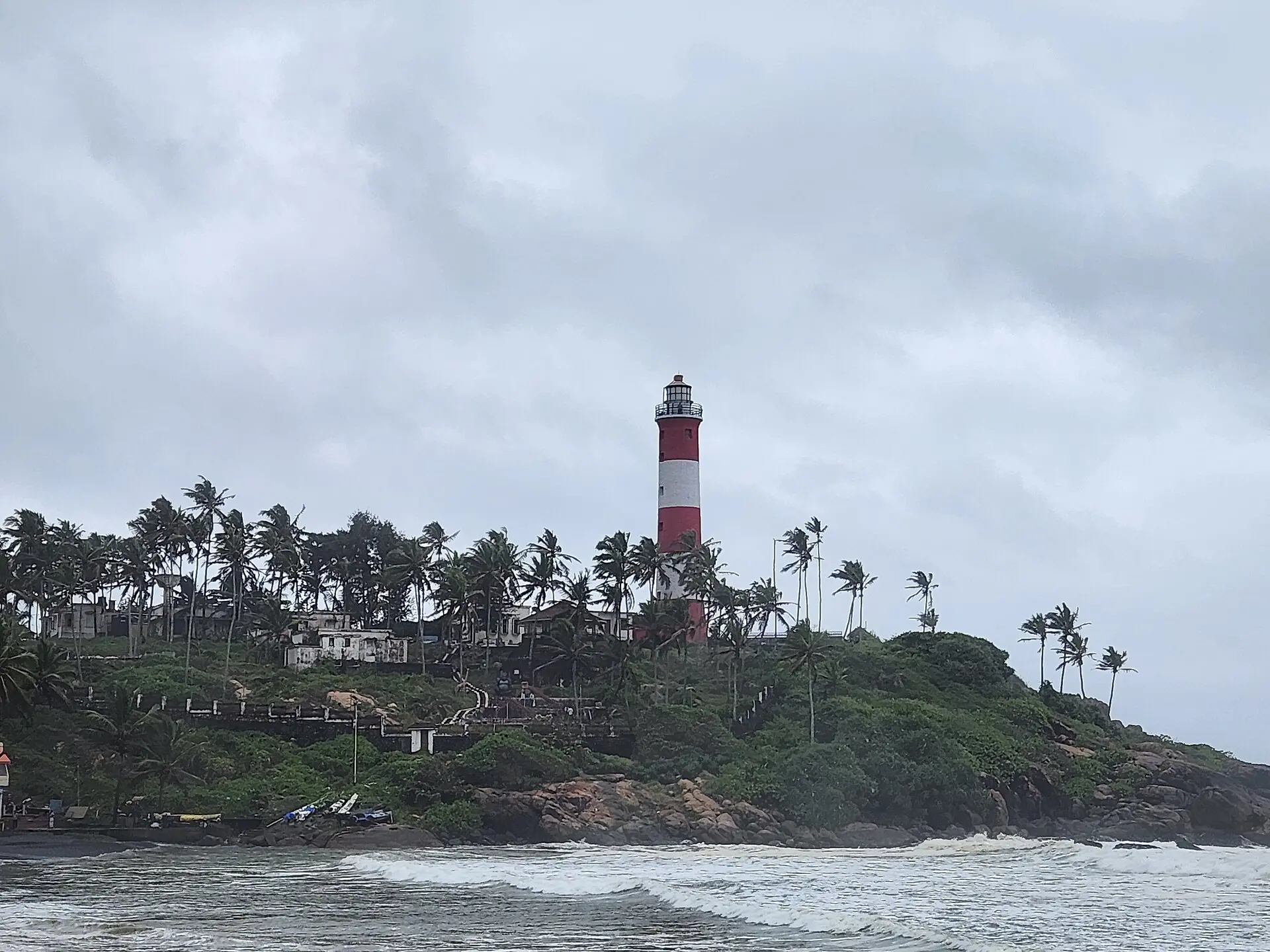 The red-and-white striped Kovalam lighthouse above palm trees on a monsoon morning