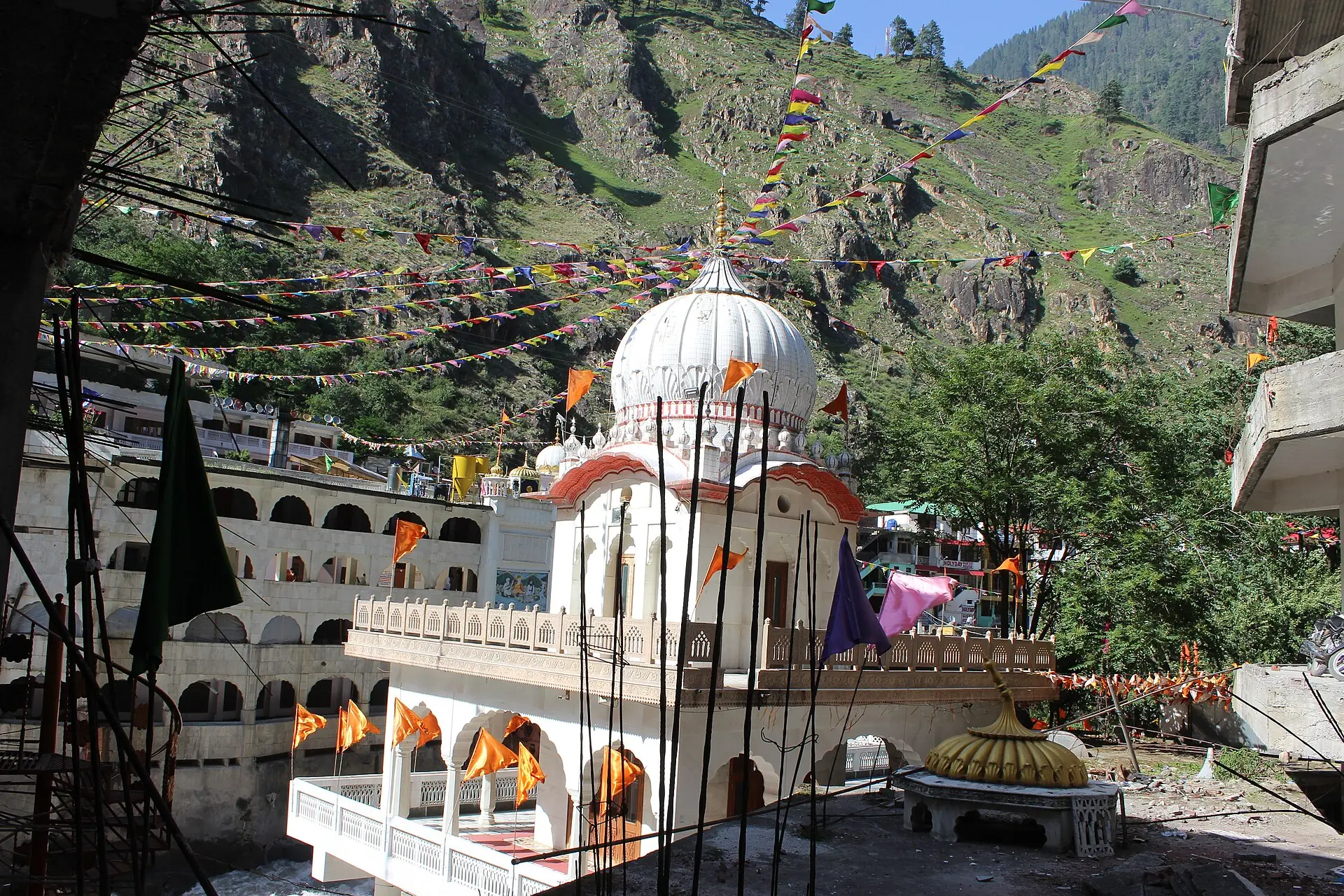 The white gurdwara at Manikaran Sahib with steep green mountains behind