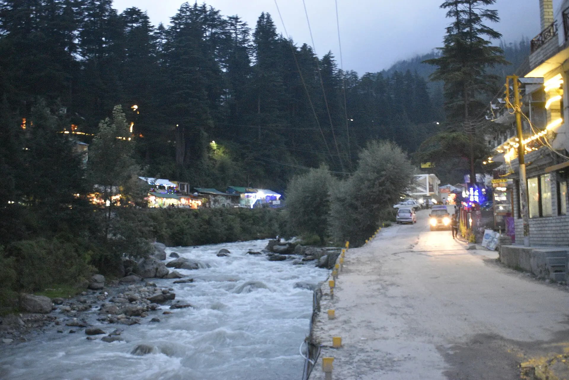 A street in Old Manali beside a rushing stream at dusk